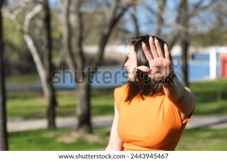Pretty young woman, brunette and orange dress puts her hand in front of her face to protect herself. The girl smiles and feels ashamed. Focus on the hand with calluses and corns