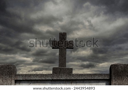 A stone cross standing on a stand of unshaken stone and storm clouds drifting over it. Royalty-Free Stock Photo #2443954893