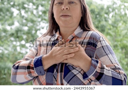 woman 45-50 years old in plaid shirt holds to heart, sudden chest pain, close up female face with facial expression suffering, Ischemic heart disease, Arterial hypertension, Myocarditis or Arrhythmia Royalty-Free Stock Photo #2443955367