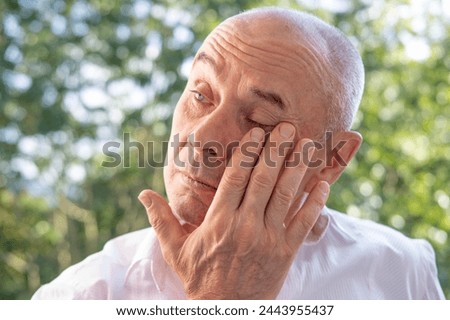 man 60-65 years old, senior crying, suffering, fatigue syndrome eye Asthenopia, eye pain symptoms, including strain, allergies, severe eye conditions, corneal ulcers, glaucoma or acute angle-closure Royalty-Free Stock Photo #2443955437