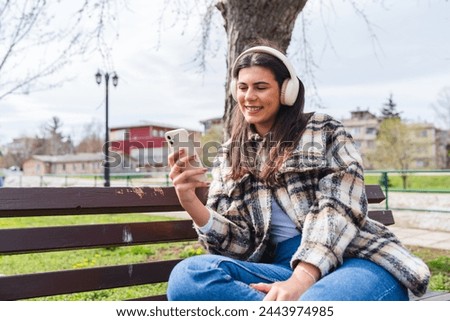 One young girl is listening to music on her wireless headphones and using her phone outdoors on a sunny day	