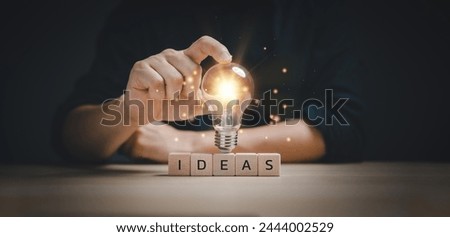 hand touching on light bulb on wood block with Word Ideas, new idea concept with innovation and inspiration, innovative technology in science and communication concept. Royalty-Free Stock Photo #2444002529