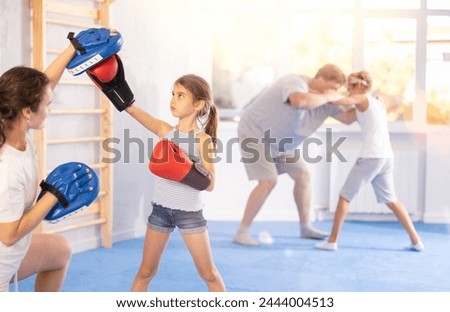 Mother and girl are engaged during training, boxing classes. Parent helps daughter master basic wrestling skills. Mom and daughter kids amateurs master boxing and practice basic strikes, hooking