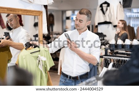 Man buys blouses for girl in clothing store and photographs goods, broadcasts assortment of department via video communication. Remote shopping, friend makes purchases for mom.