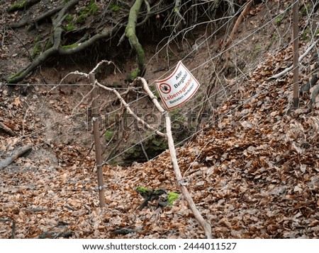 Collapsed entrance of an old mine with a danger sign "Lebensgefahr - Betreten verboten!" (danger to life  - no trespassing) in a forest in Germany. Dangerous holes in the ground.