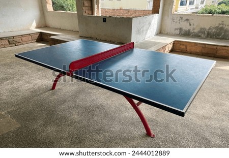 Interior photo visual view of a table tennis or ping pong table with a red solid net in a room in blue color surface with nobody playing in an open space area shared with everybody who wants to play