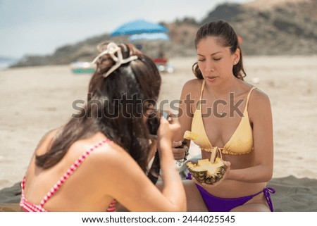 Two latin young female friends taking pictures of a beach picnic during holidays