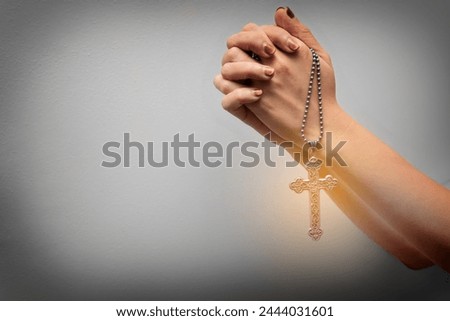 Female hands praying holding a silver vintage rosary on white background with yellow spot on rosary. Easter festival. Faith. Christian. Jesus