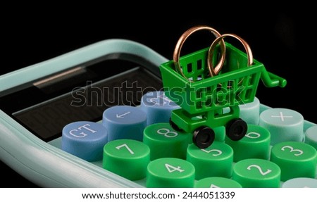 Wedding rings in miniature shopping cart and calculator on black background