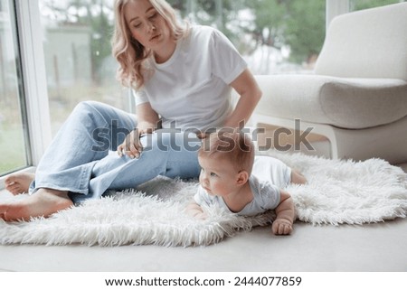 A 5-month-old baby and his  beautiful blonde mom relax, play and laugh in bed in the bedroom. People a dressed in light home clothes, the family chooses natural textiles
