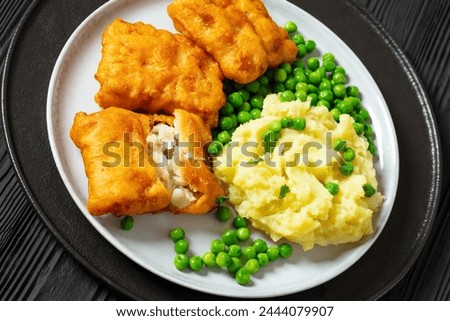 crispy fried fish fillet with mashed potatoes and green peas on plate, close-up, dutch angle view Royalty-Free Stock Photo #2444079907