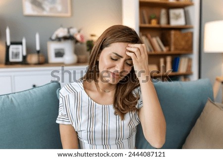 Headache. Close-up photo of a young woman, who is sitting on a sofa , touching her head while suffering from a migraine.