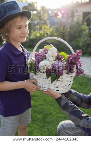 6-year-old boy gives a wicker basket with flowering branches of white and purple lilacs as a gift to his mother or grandmother. festive mood. sunny backlighting. Mothers Day, selective focus