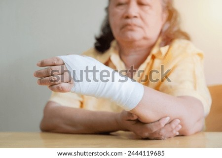 Asian old woman arm with gauze bandage on it. Sprain, stress fracture or repetitive strain injury in hand. Selective focus. Royalty-Free Stock Photo #2444119685