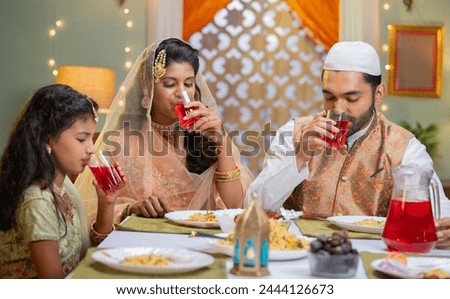 Indian Muslim couple with kid having juice or rooh afza during ramadan festival celebration at home - concept of ramadan iftar, family bonding and tradition Royalty-Free Stock Photo #2444126673