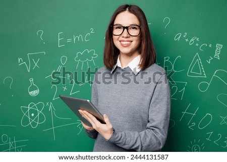 Young smiling smart IT teacher woman wear grey casual shirt glasses use digital tablet pc computer isolated on green wall chalk blackboard background studio. Education in high school college concept