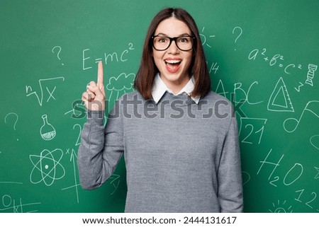 Young smart teacher woman wear grey casual shirt glasses holding index finger up with great new idea isolated on green wall chalk blackboard background studio. Education in high school college concept