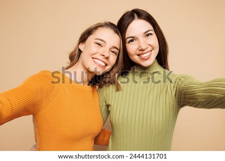 Close up fun young friends two women they wear orange green shirt casual clothes together doing selfie shot pov on mobile cell phone isolated on plain pastel light beige background. Lifestyle concept