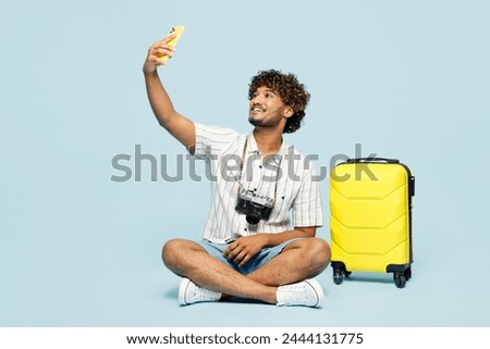 Full body traveler man wear white casual clothes sit near bag do selfie shot on mobile cell phone isolated on plain blue background. Tourist travel abroad in free time rest getaway. Air flight concept