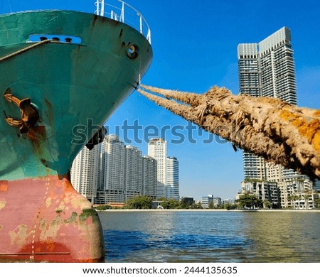 Anchor on large cargo ship's anchor being pulled. Blue and red ship, While docked at the pier by large ropes on the river, in the background is a view of the city's buildings and transport concept
