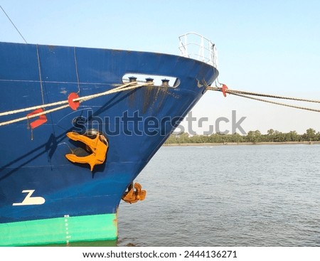 Anchor with side of large cargo ship, anchor being pulled. Blue and green ship, While docked at the pier by large ropes on the river, in the background is a view of the blue sky and transport concept