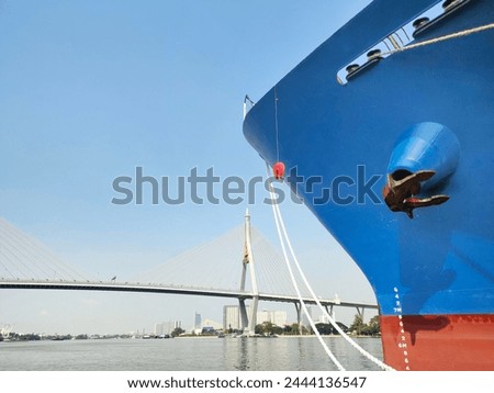 Anchor with large cargo ship's, anchor being pulled. Blue and red ship, While docked at the pier by large ropes on the river, in the background is a view of the city's buildings and transport concept