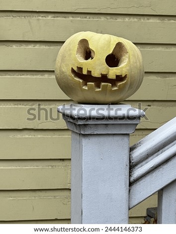 An eye level view of a yellow Jack-o'-lantern displayed on the end post of stairs with a background of yellow wooden sidings
