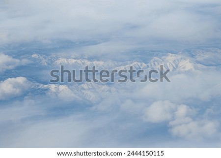 Top view of snow-capped mountains. Snow-covered mountain peaks among the clouds. Beautiful aerial landscape. Great for background. Khabarovsk region, Russia. Royalty-Free Stock Photo #2444150115