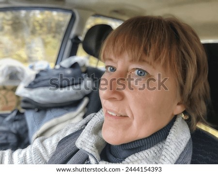 Funny cute blonde girl or a middle-aged woman driving a car in summer, autumn, spring day. A female driver on a solo trip