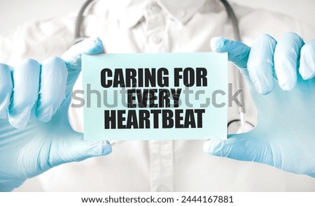 Hands in blue gloves holding a sign CARING FOR EVERY HEARTBEAT .