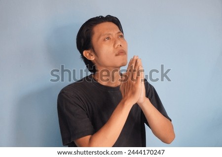 Handsome Asian young man wearing black t-shirt praying with hands together asking for forgiveness