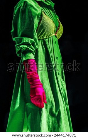 Interesting creative bright outfit green dress, pink gloves on black background