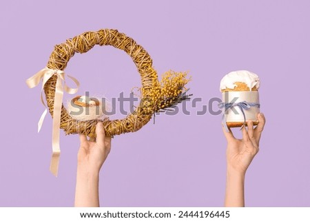 Female hands holding Easter cake with wreath on lilac background