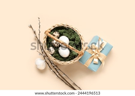 Wicker basket with Easter eggs, pussy willow branches and gift box on beige background