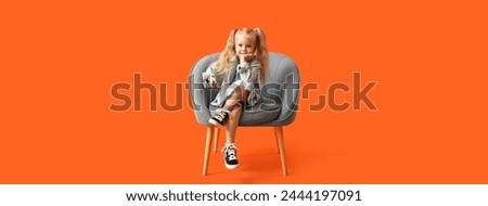 Little girl in armchair watching TV on orange background