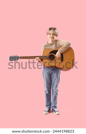 Cute little boy playing guitar on pink background