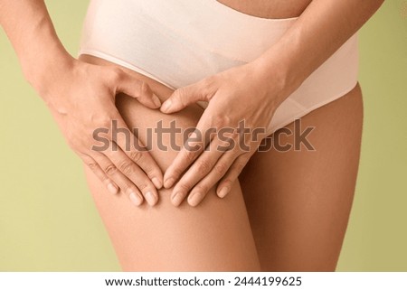 Beautiful young African-American woman with stretch marks on her body showing heart gesture against green background, closeup