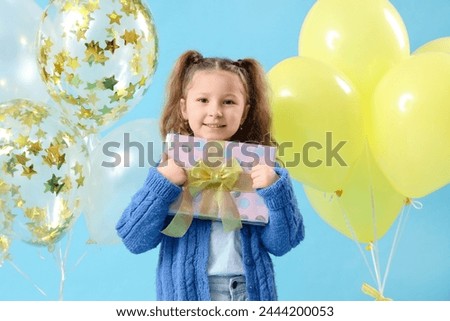 Cute little girl with balloons and gift box on blue background