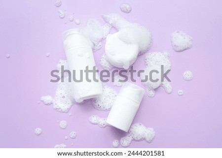 Bottles of cosmetic products with foam on lilac background