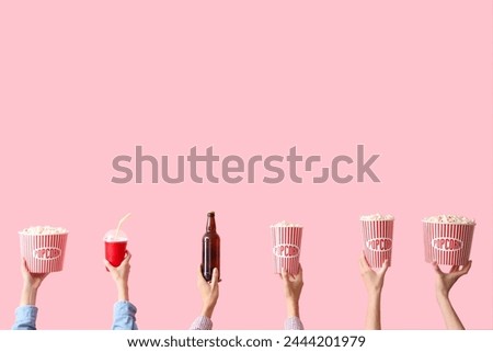Hands with buckets of popcorn, beer and drink on pink background
