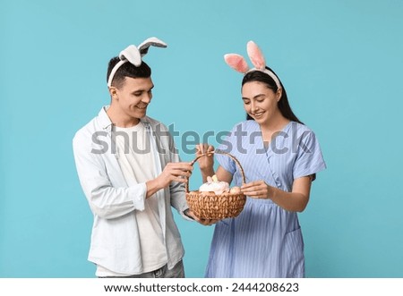 Happy young couple with Easter bunny ears and basket on blue background
