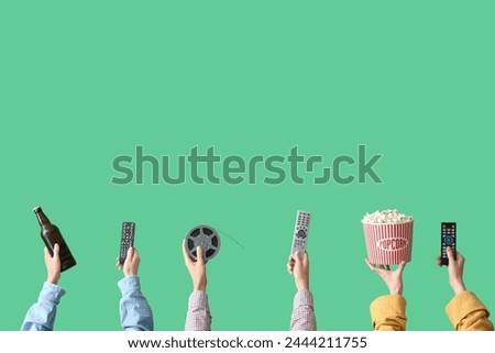 Many hands with bucket of popcorn, beer and TV remotes on green background