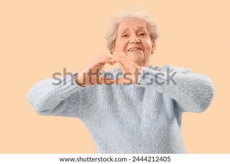 Senior woman making heart with her hands on beige background