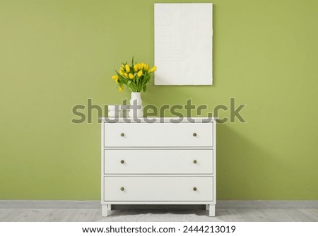 Beautiful vase of yellow tulips on chest of drawers and picture on wall in living room