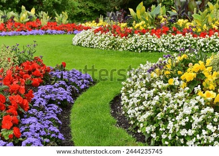 Scenic view of colourful flowers in bloom and a winding grass lawn path in a beautiful English style landscape garden on a summer day