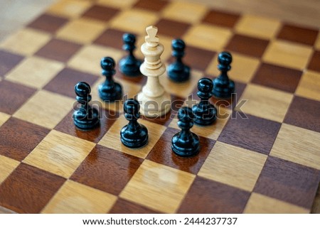 White chess king surrounded by black pawns on wooden chess board Royalty-Free Stock Photo #2444237737