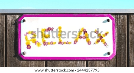 word RELAX from yellow, pink flowers collage, enamel, metal, elongated stone pottery relax sign on a rustic wooden wall. pink frame, turquoise sky, sun shining, floral letter, spa wellness relaxation