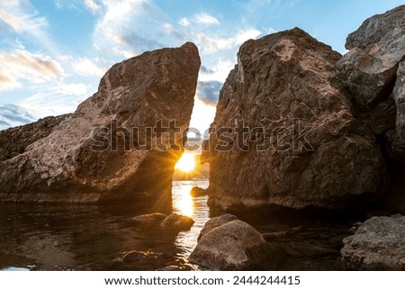 Sudak, Crimea. Sunset over the waters of the Black Sea. The ship against the backdrop of the sun. Rocks and backlight. Contrasting and bright sky with clouds Royalty-Free Stock Photo #2444244415