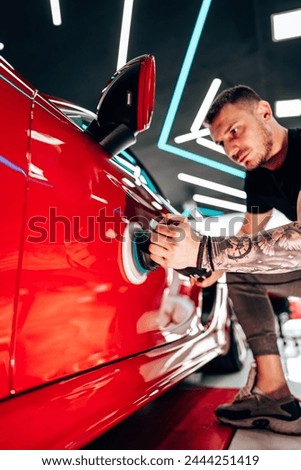 Professional vehicle polishing and detailing service in a modern car workshop. Brightly lit workspace with large led lights. High quality car valeting concept. Royalty-Free Stock Photo #2444251419