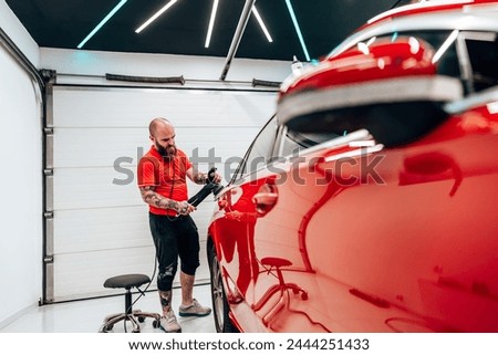 Professional vehicle polishing and detailing service in a modern car workshop. Brightly lit workspace with large led lights. High quality car valeting concept. Royalty-Free Stock Photo #2444251433